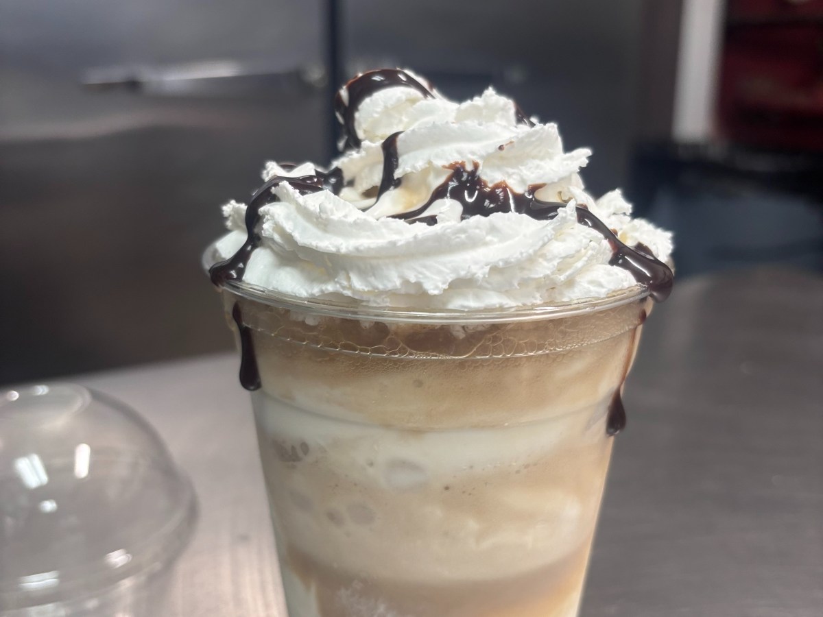 Iced coffee in a clear cup topped with whipped cream and chocolate drizzle.