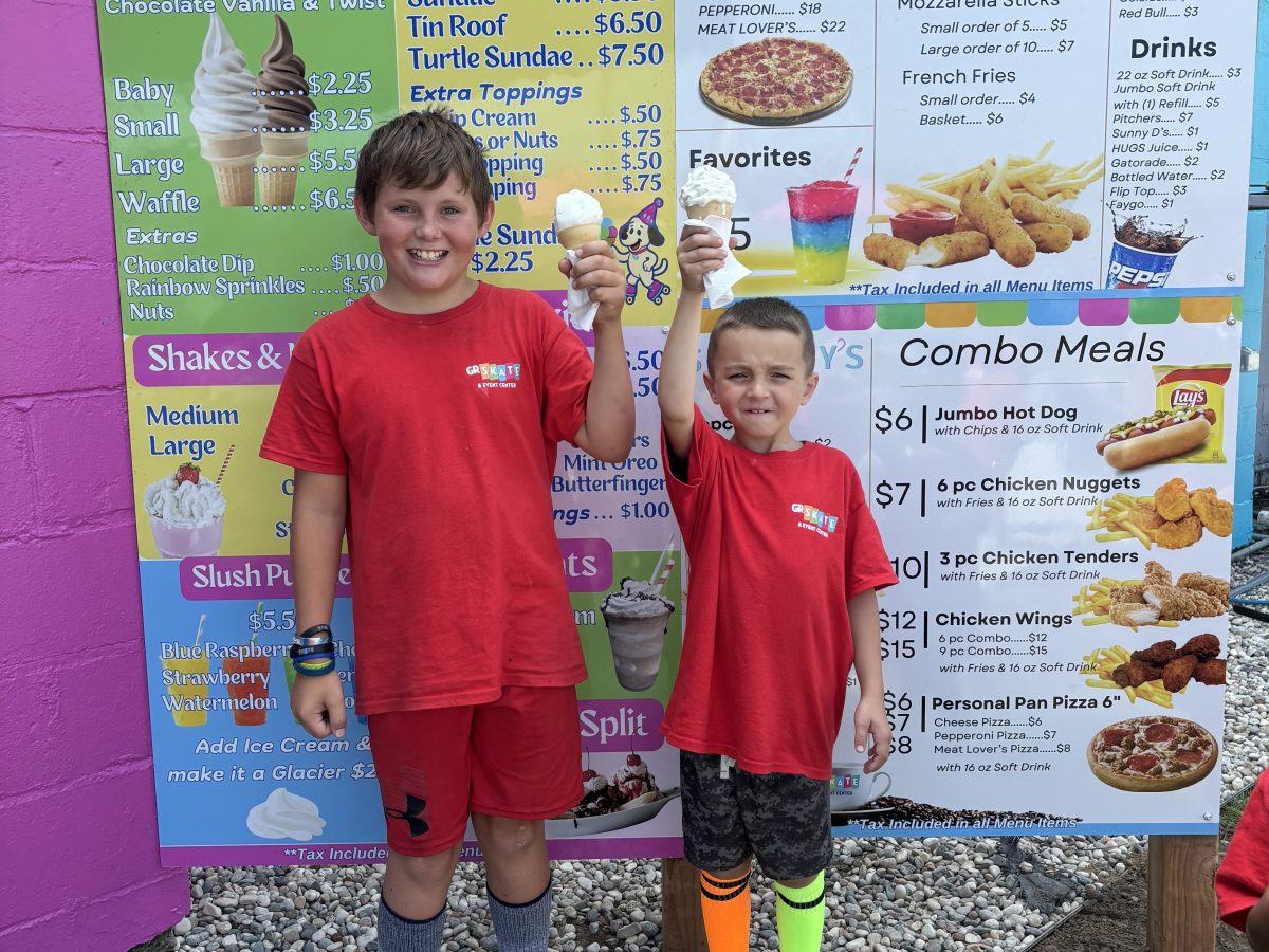 Two kids in red shirts holding ice cream cones in front of a colorful menu board.