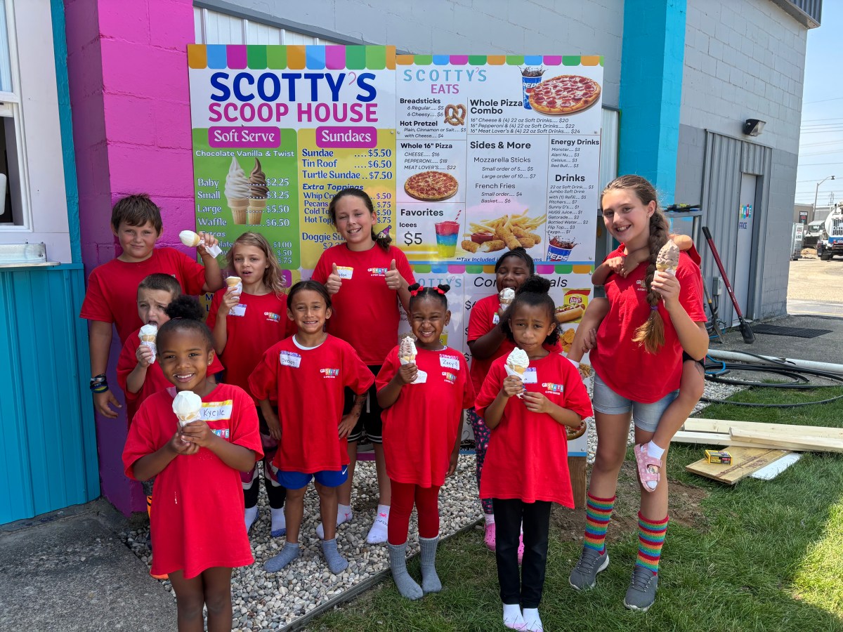 Group of kids in red shirts holding ice cream in front of a colorful menu board.
