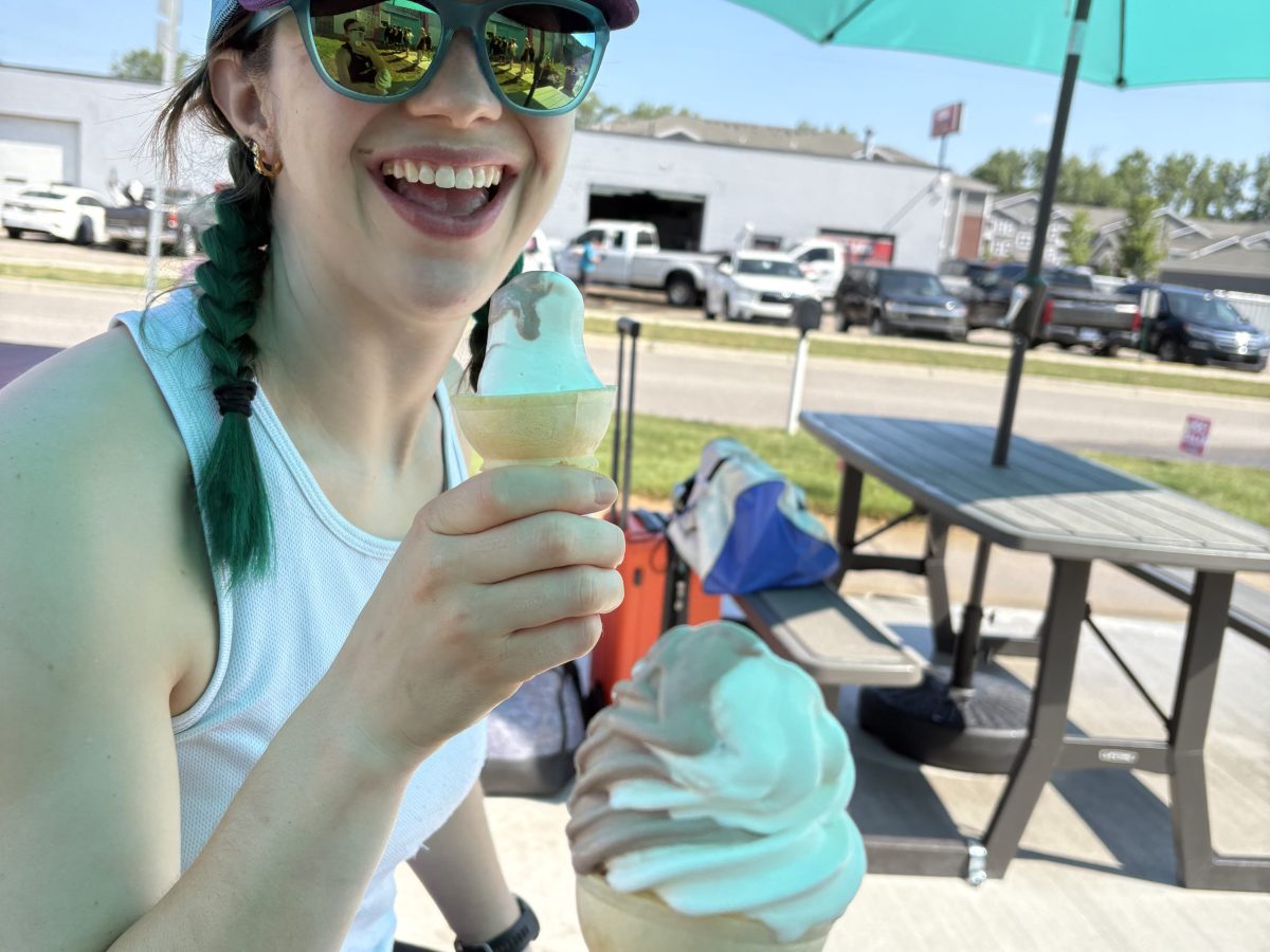 Person smiling with blue cap holding ice cream cone under colorful umbrellas.