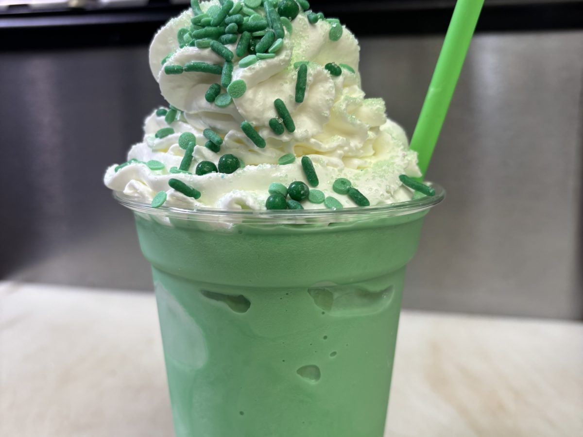 Green milkshake with whipped cream and green sprinkles, topped with a green straw.