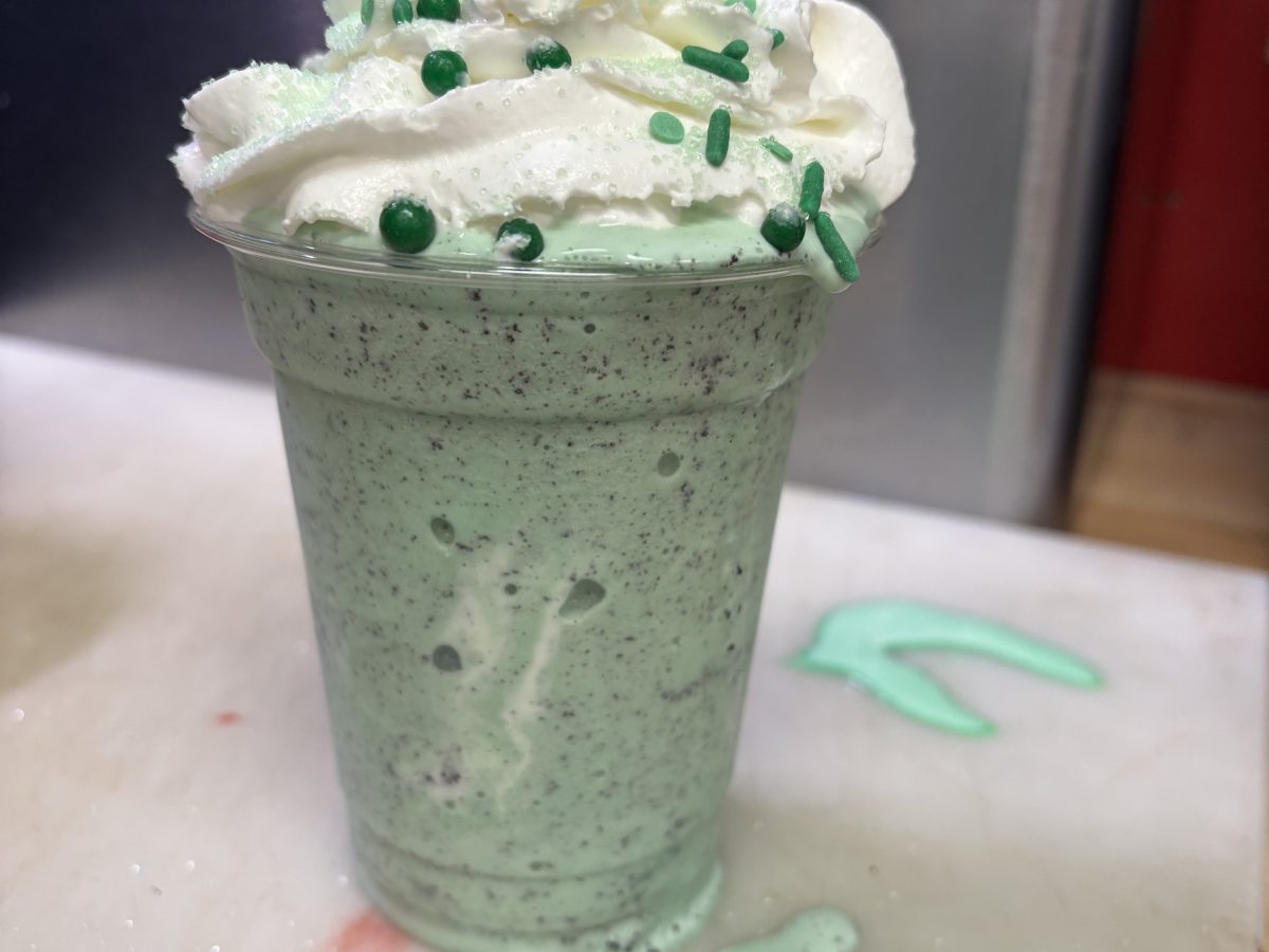 Mint chocolate milkshake with whipped cream, green sprinkles, and a cookie on top.