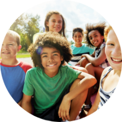 Group of smiling children sitting outdoors on a sunny day.