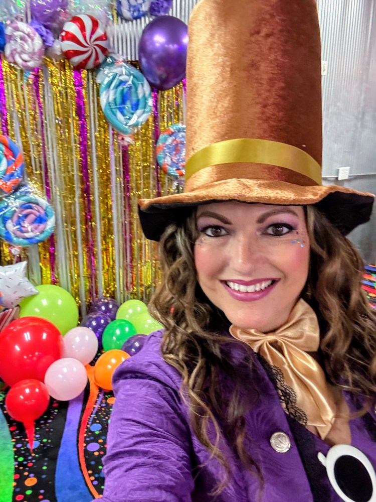 Person in a tall hat and costume, surrounded by colorful balloons and decorations.