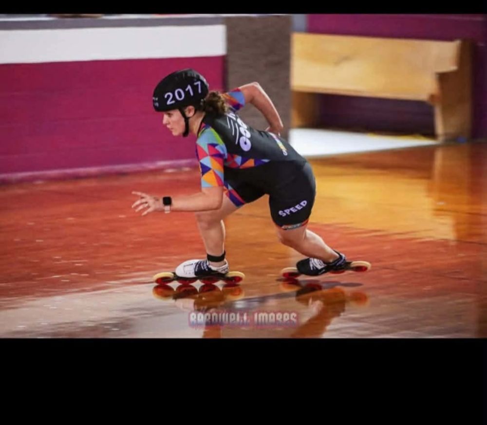 Person in helmet and skates racing indoors on a polished floor.