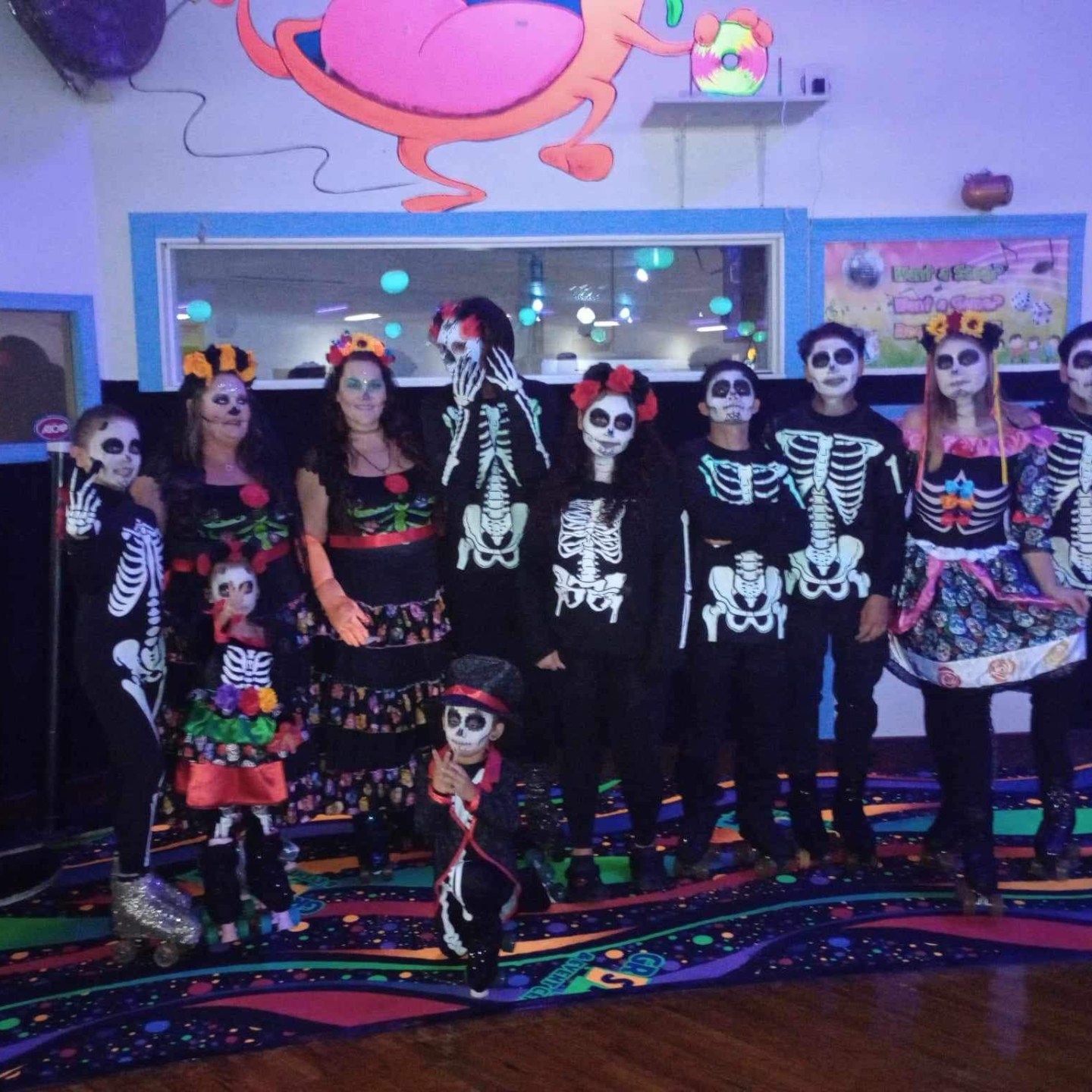 Group in skeleton costumes with face paint posing indoors at a themed party.