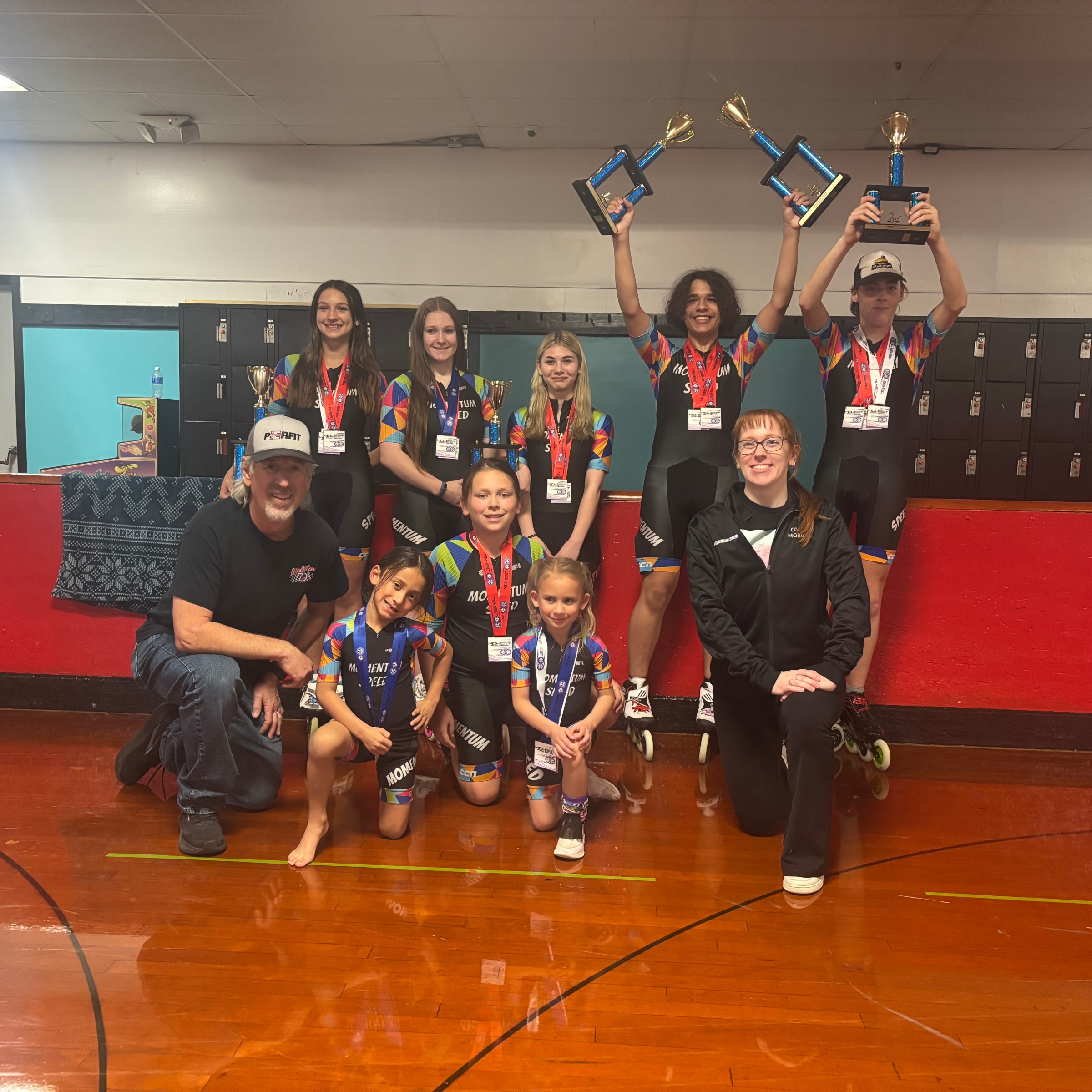 Group of people, including children, in sports attire holding trophies indoors.