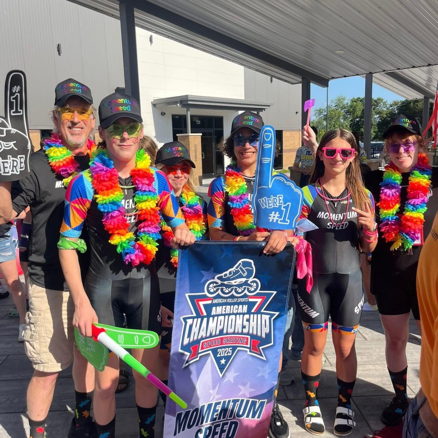 Group in rainbow leis and hats celebrate with a championship banner.