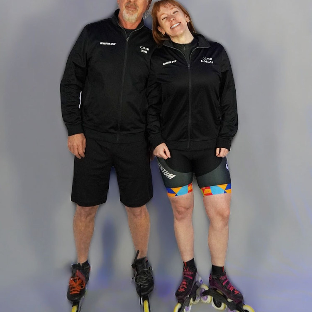 Two people in black sportswear and rollerblades smiling at the camera.