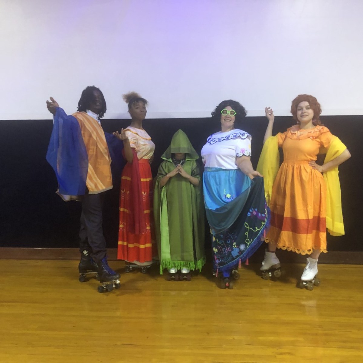 Five people in colorful costumes posing on roller skates on stage.