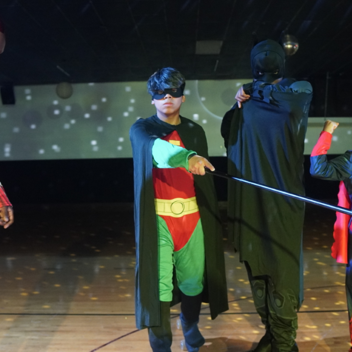 Four people in superhero costumes pose in a dimly lit room.