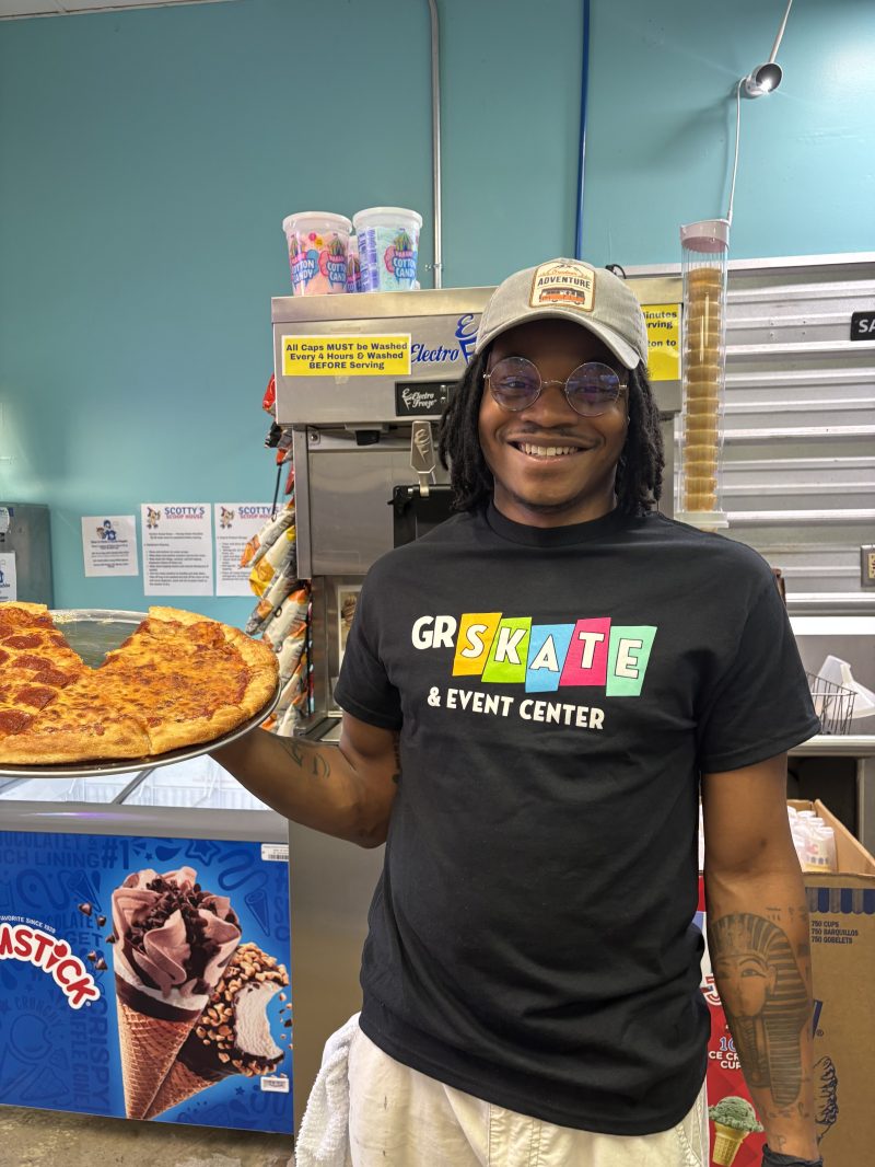 Person holding a large slice of pizza in an ice cream shop.