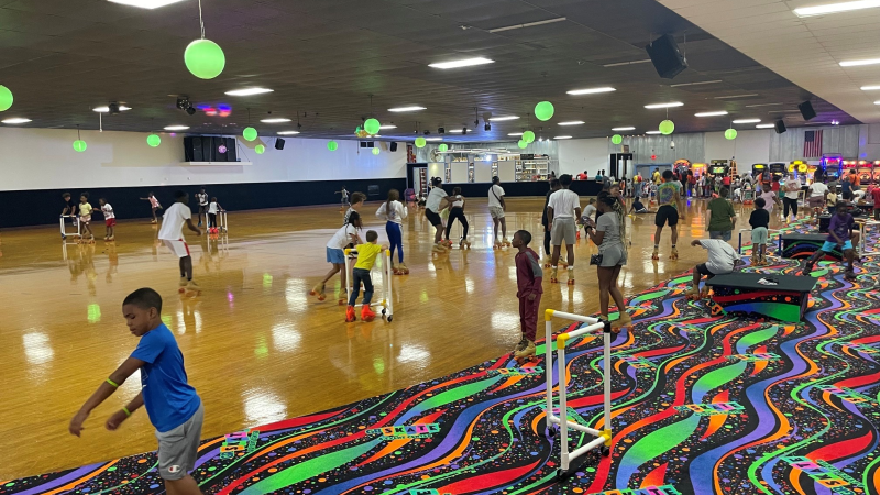 Kids and adults roller skating indoors on a colorful rink with neon decorations.