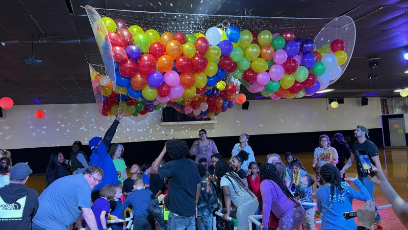 Group of people under colorful balloons caught in a net at a party.