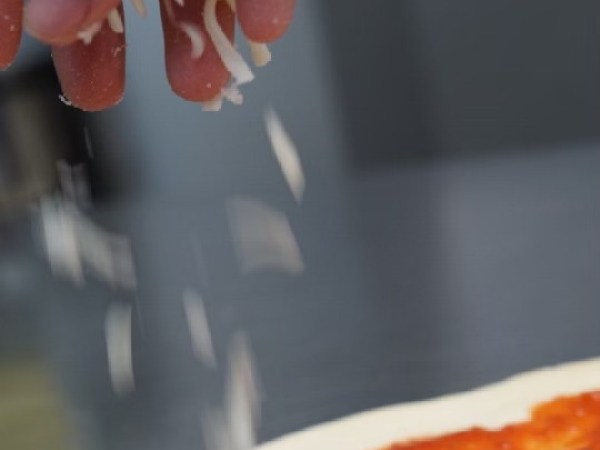 Hand sprinkling cheese on a tomato sauce-covered pizza crust.