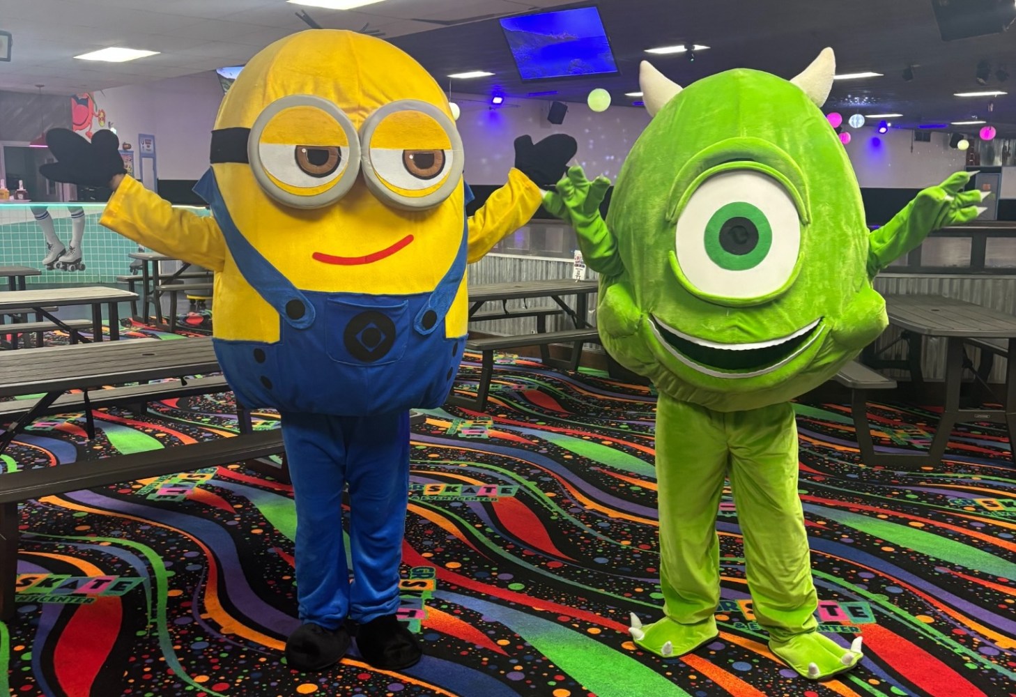 Two people in cartoon character costumes posing inside a colorful, arcadelike setting.