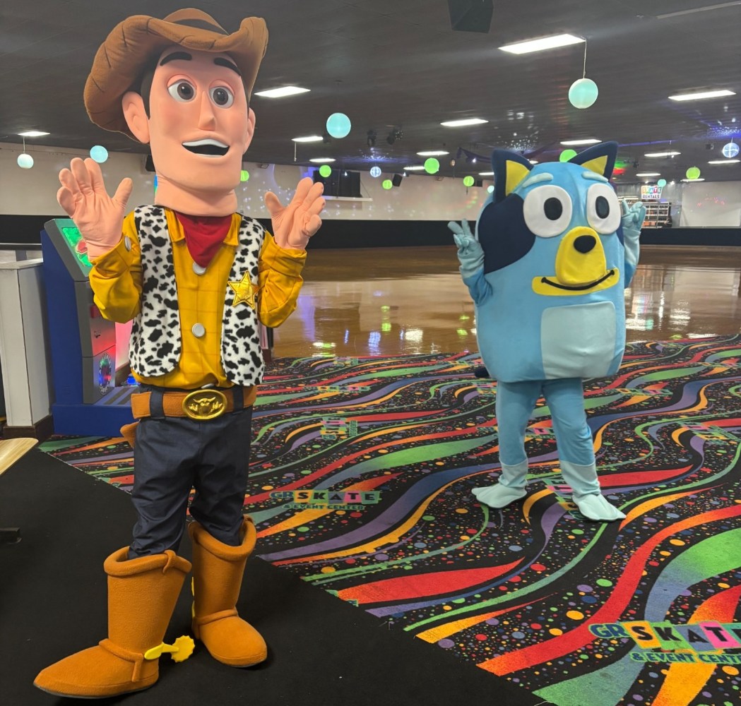 Two cartoon character mascots in colorful costumes on a vibrant, patterned floor.